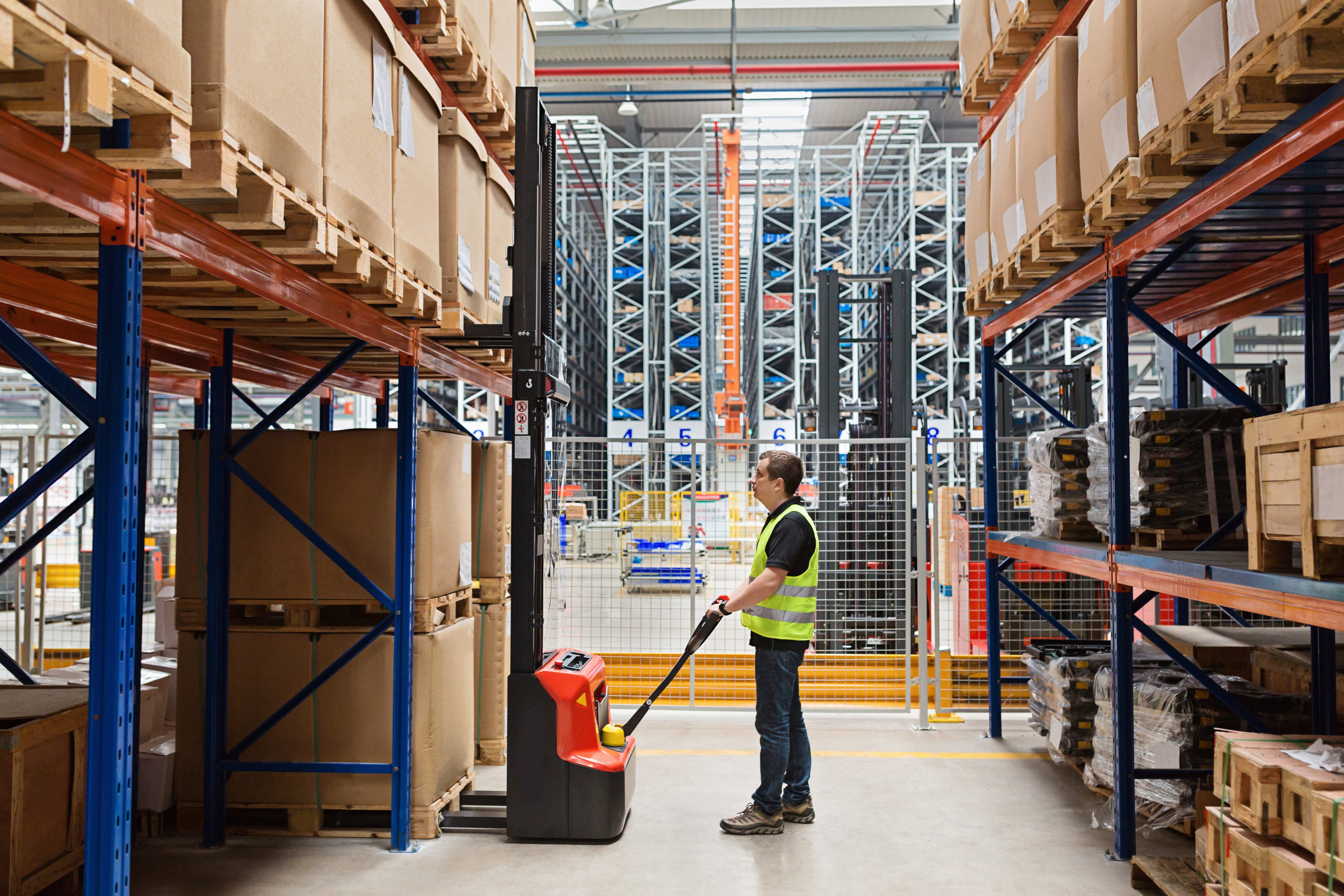 Storehouse man employee in uniform using forklift with box in modern automatic warehouse. Boxes are on the shelves of the warehouse. Warehousing, machinery concept. Logistics in stock.